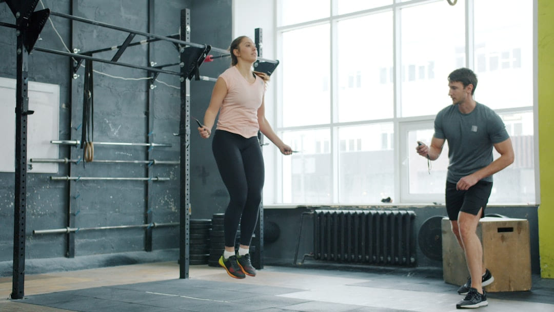 Woman jumps rope while man watches in gym. on First Rep Forward